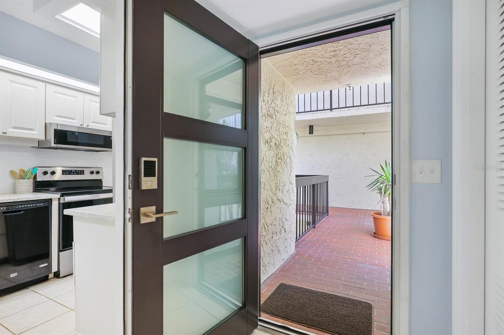 An open door reveals a kitchen with white cabinets and a brick-paved outdoor balcony — 1935 GULF OF MEXICO DRIVE UNIT G7-304, LONGBOAT KEY, FL