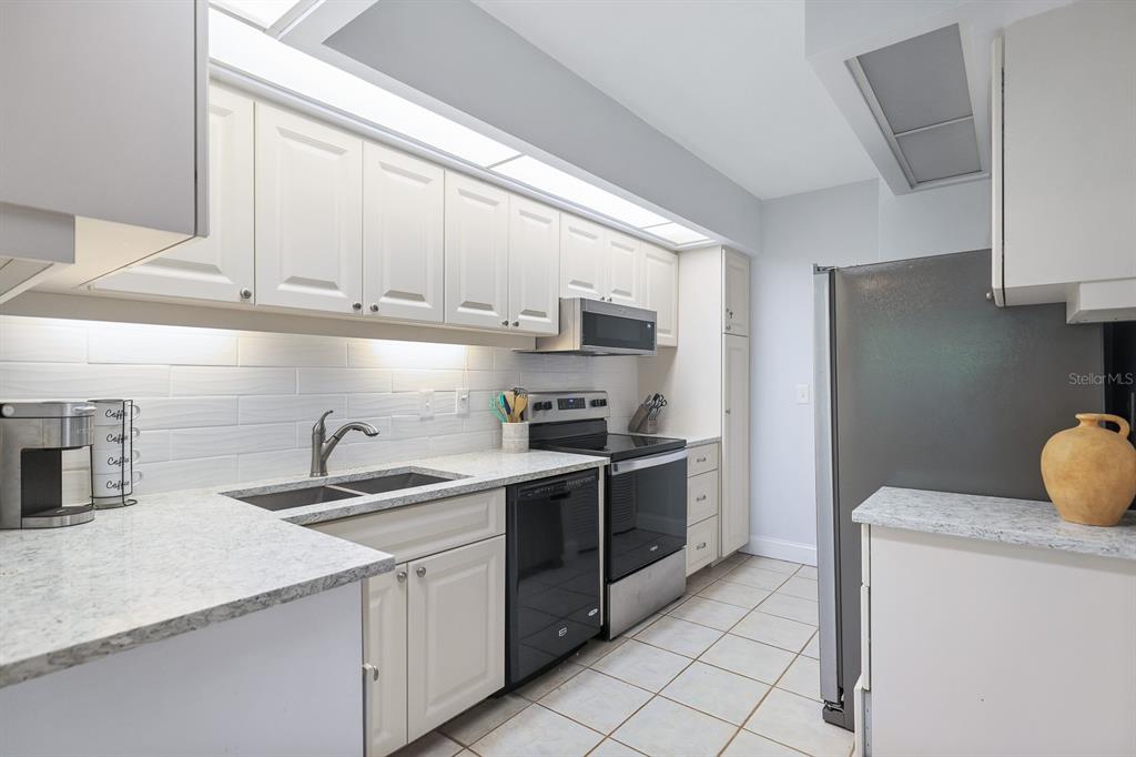 A kitchen features white cabinets, granite countertops, a tiled backsplash, and stainless steel appliances — 1935 GULF OF MEXICO DRIVE UNIT G7-304, LONGBOAT KEY, FL