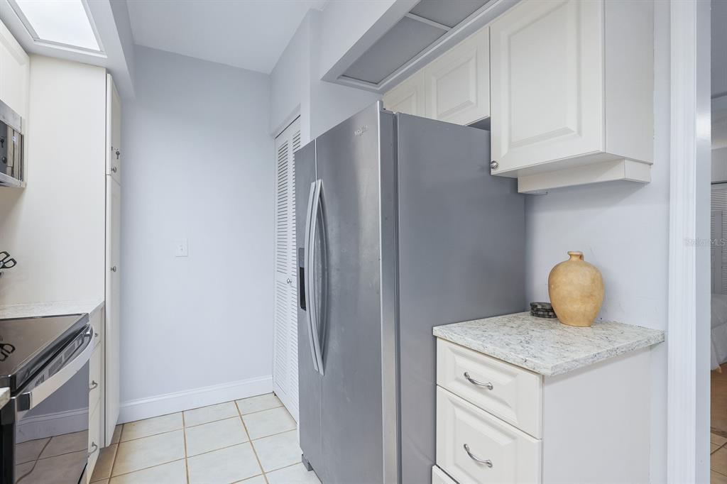 A kitchen features white cabinets, granite countertops, a stainless steel refrigerator, and tiled flooring — 1935 GULF OF MEXICO DRIVE UNIT G7-304, LONGBOAT KEY, FL