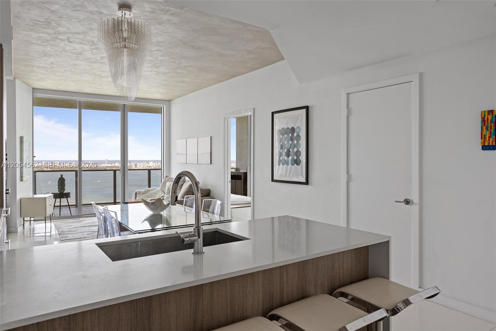 A modern kitchen island with a sink overlooks a dining area and a balcony view — 2900 NE 7th Ave # 4205, Miami FL 33137, MIAMI, FL