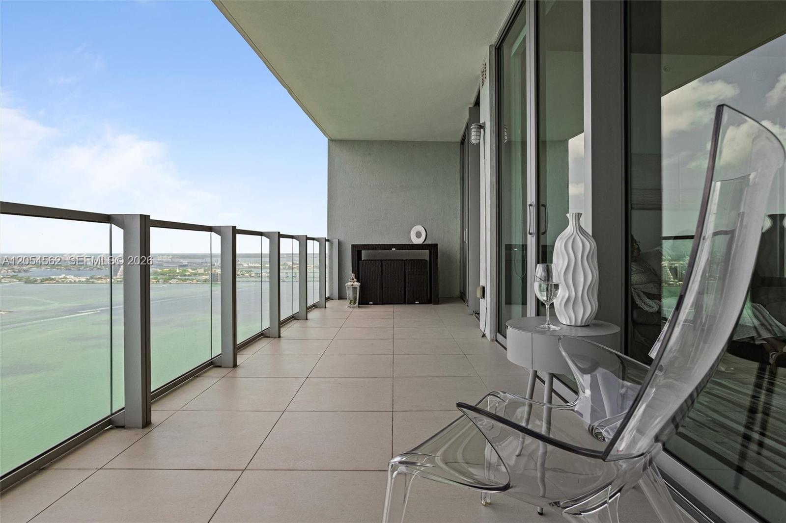 A balcony with glass railings overlooks a body of water and features a transparent chair — 2900 NE 7th Ave # 4205, Miami FL 33137, MIAMI, FL