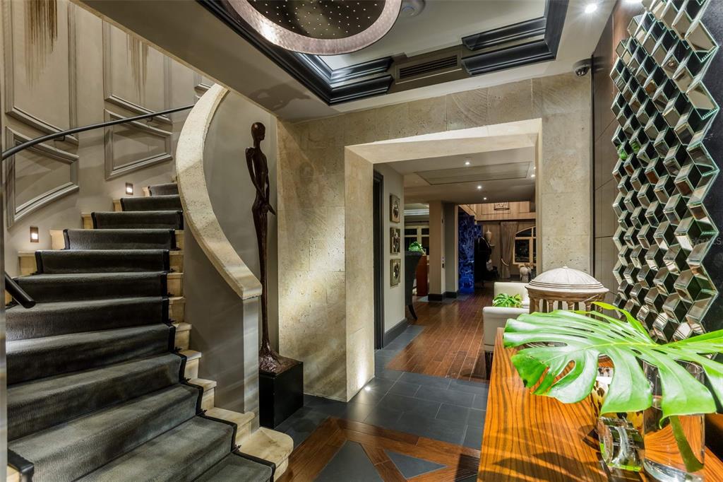 A grand foyer features a curved staircase, stone walls, a decorative mirror wall, and wood flooring — 500 PLANTATION DRIVE UNIT PH-3403, DORADO, PR