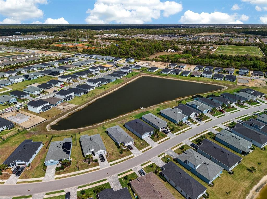 An aerial view shows a suburban neighborhood with houses surrounding a large retention pond — 16390 QUEEN PALM DRIVE, PORT CHARLOTTE, FL