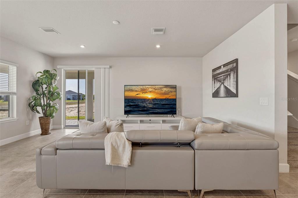 A living room features a grey sectional sofa, a television on a white stand, and tile flooring — 16390 QUEEN PALM DRIVE, PORT CHARLOTTE, FL