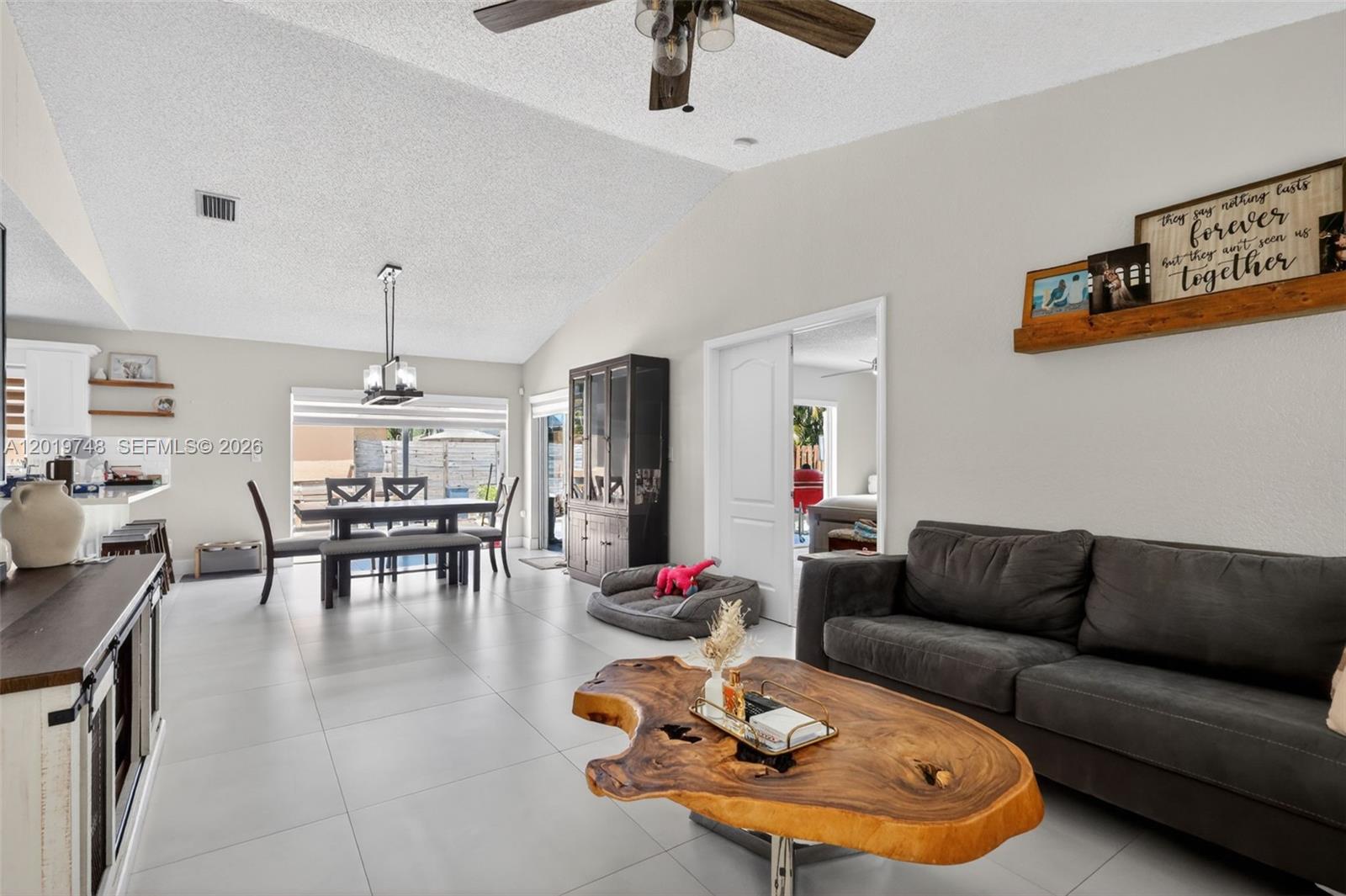 A living and dining area features a live-edge coffee table, gray sofa, and vaulted ceilings — 8061 NW 197th St, Hialeah FL 33015, HIALEAH, FL