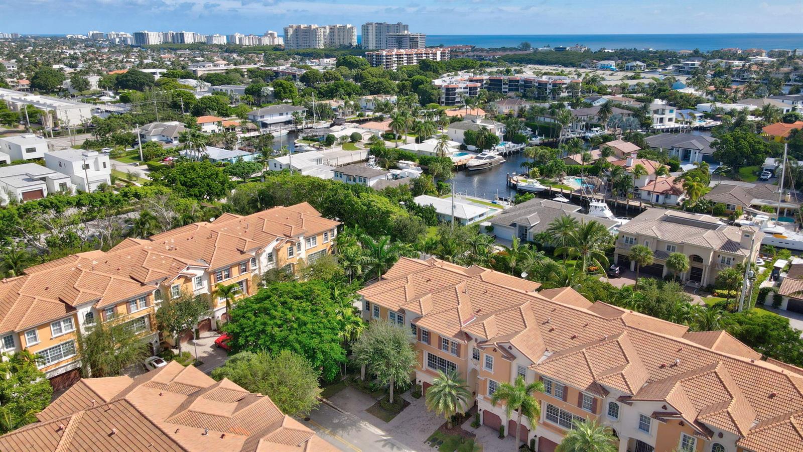 An aerial view shows multi-story townhomes with terracotta roofs near a canal and ocean — 5660 NE Trieste Way, Boca Raton FL 33487, BOCA RATON, FL