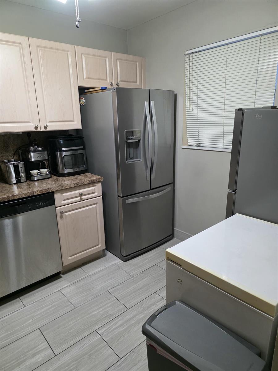 A kitchen features light wood cabinets, stainless steel appliances, and gray tile flooring — 3130 Holiday Springs Boulevard # 307, Margate FL 33063, MARGATE, FL