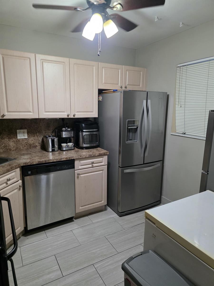 A kitchen features light wood cabinets, stainless steel appliances, and gray tile flooring — 3130 Holiday Springs Boulevard # 307, Margate FL 33063, MARGATE, FL
