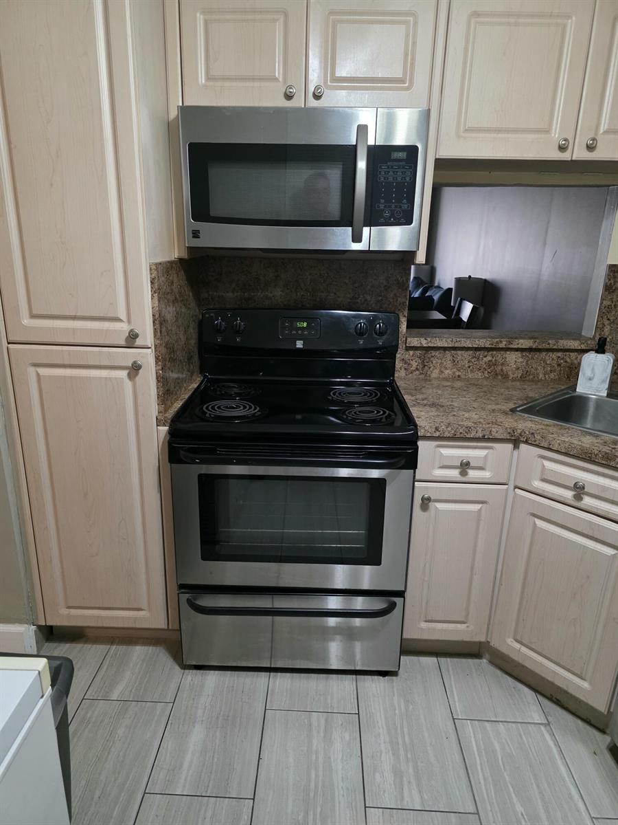 A kitchen features light wood cabinets, stainless steel appliances, and a black electric range — 3130 Holiday Springs Boulevard # 307, Margate FL 33063, MARGATE, FL