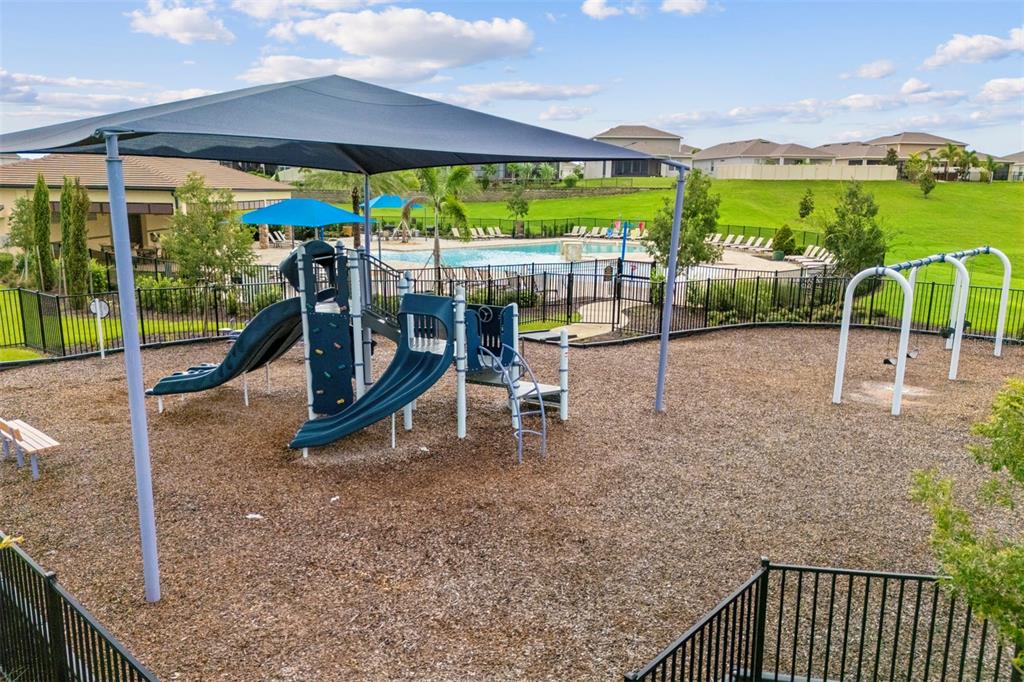 A playground with a shade structure, slides, and swings sits next to a swimming pool — 7500 CATANIA LOOP, CLERMONT, FL