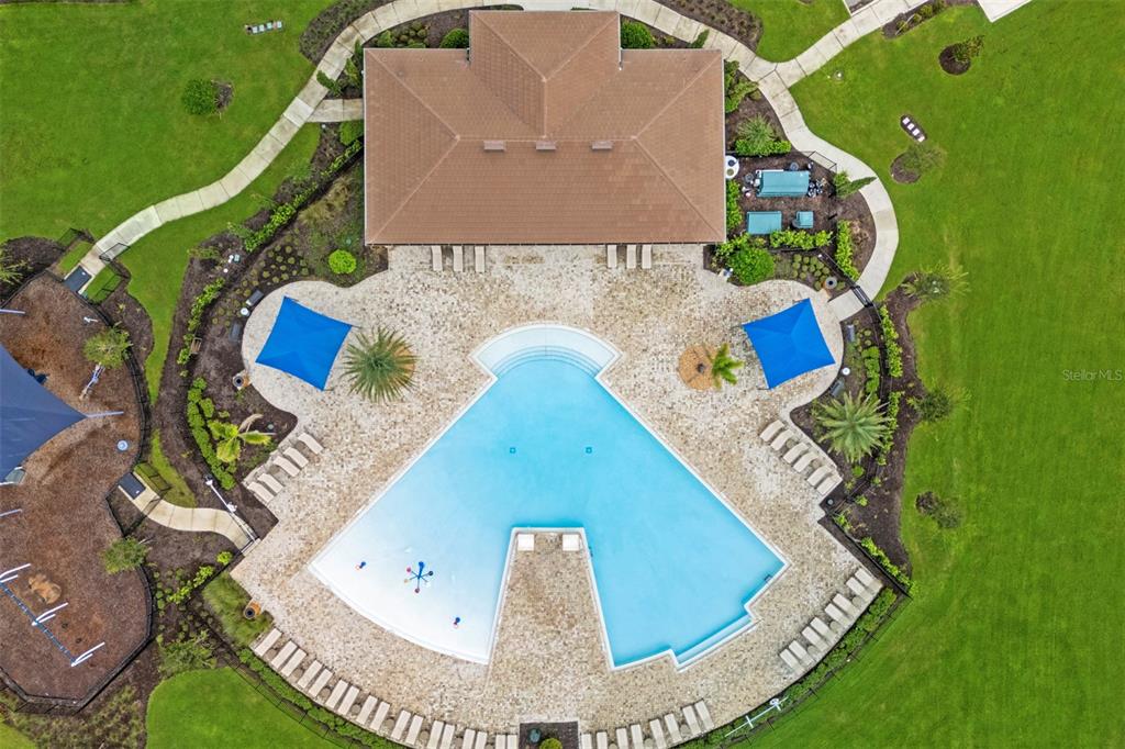 An aerial view shows a community swimming pool with lounge chairs and a clubhouse building — 7500 CATANIA LOOP, CLERMONT, FL