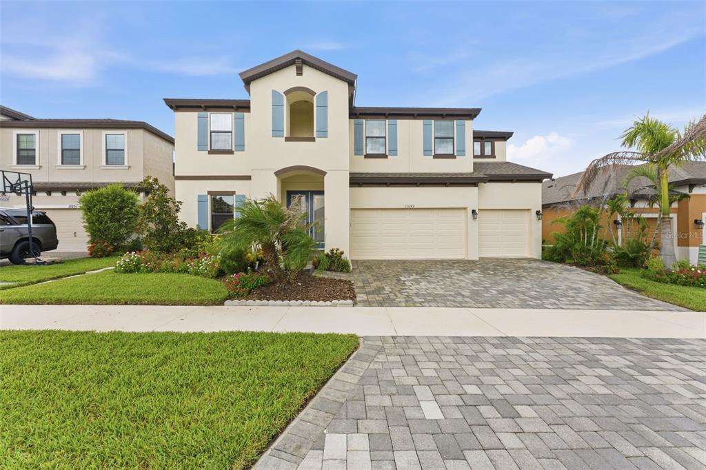 A two-story suburban house with a paved driveway, a three-car garage, and blue shutters — 13249 WILDFLOWER MEADOW DRIVE, RIVERVIEW, FL