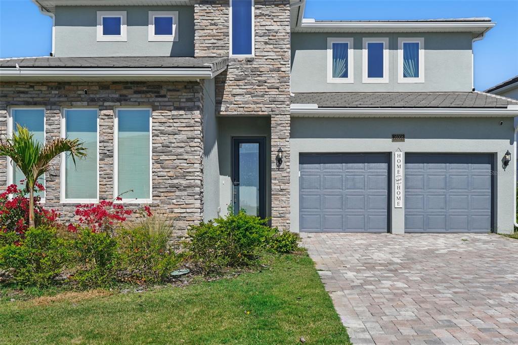 A two-story house with a stone facade, gray stucco, and a two-car garage — 16008 VOLTERRA POINT, BELLA COLLINA, FL