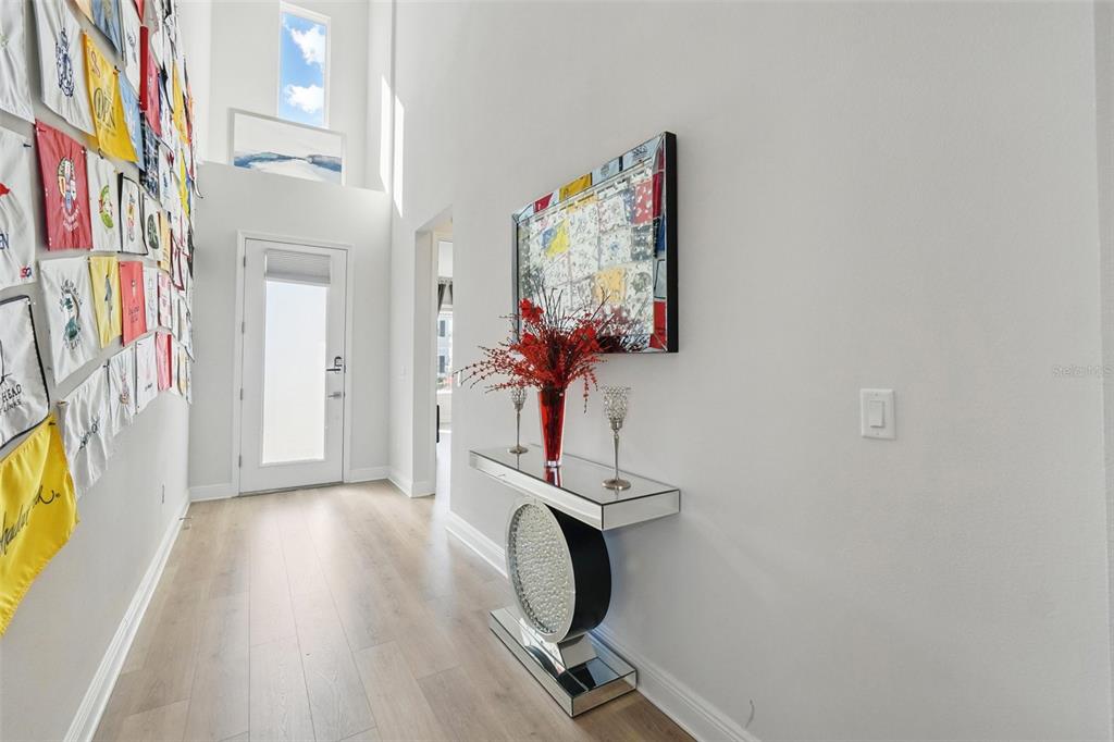 A bright entryway features light wood flooring, a mirrored console table, and a wall of flags — 16008 VOLTERRA POINT, BELLA COLLINA, FL