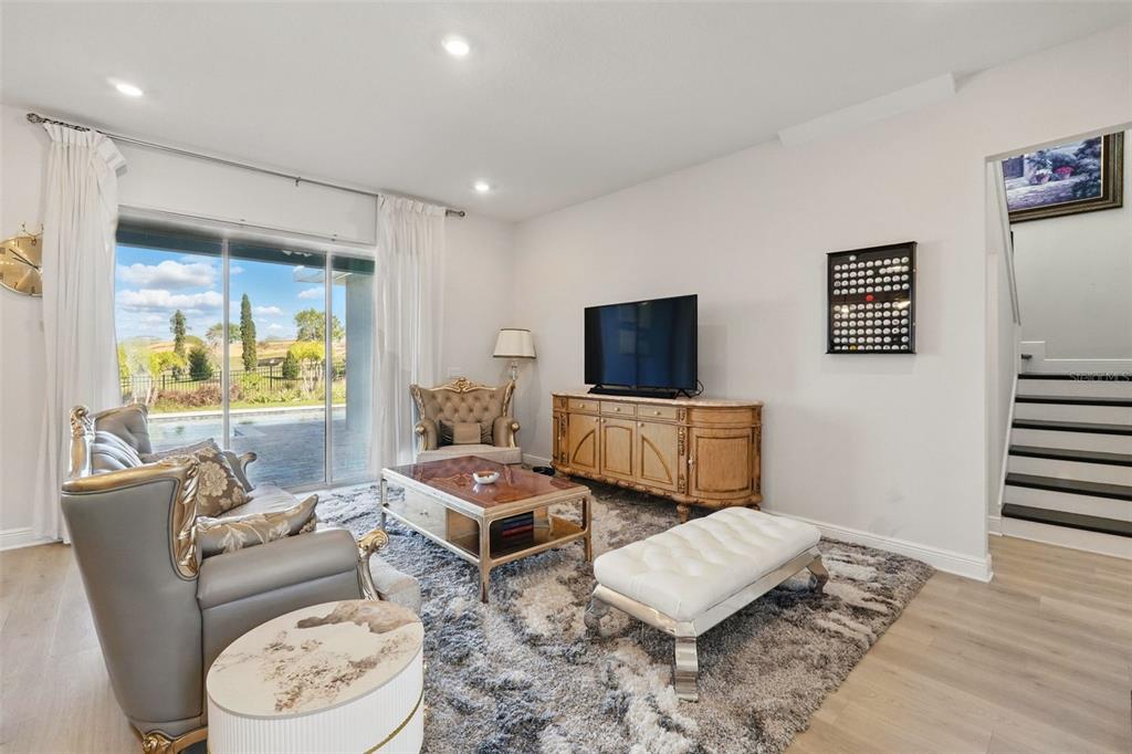A living room features a gray sofa, a wooden media console, and a sliding glass door — 16008 VOLTERRA POINT, BELLA COLLINA, FL