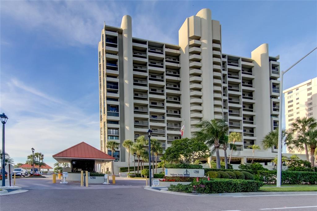 A multi-story beige residential building stands behind a gated entrance with a guardhouse — 1290 GULF BOULEVARD UNIT 1102, CLEARWATER BEACH, FL