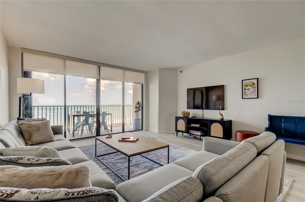 A living room features a sectional sofa, a coffee table, and a balcony with ocean views — 1290 GULF BOULEVARD UNIT 1102, CLEARWATER BEACH, FL