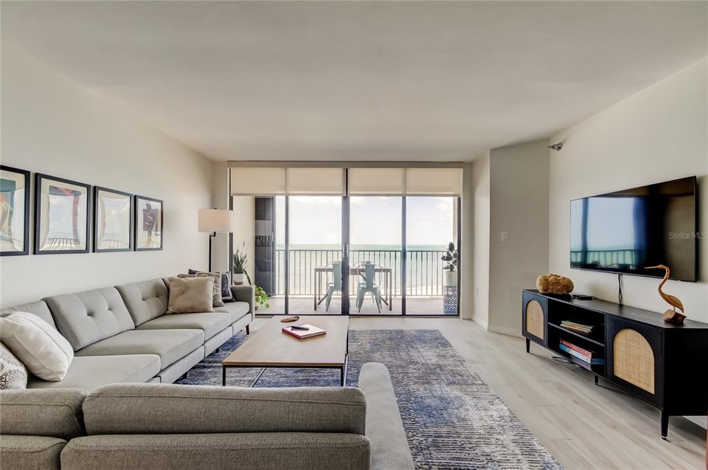 A living room features a gray sectional sofa, a television, and a balcony overlooking the ocean — 1290 GULF BOULEVARD UNIT 1102, CLEARWATER BEACH, FL