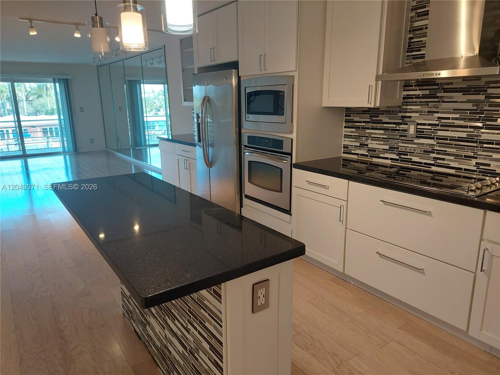 A modern kitchen features white cabinets, black countertops, stainless steel appliances, and a tiled island — FORT LAUDERDALE, FL