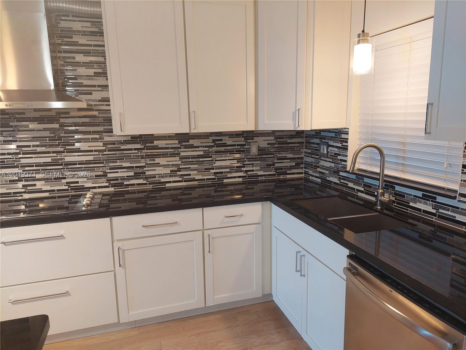 A kitchen features white cabinets, black countertops, and a multi-colored horizontal tile backsplash — FORT LAUDERDALE, FL