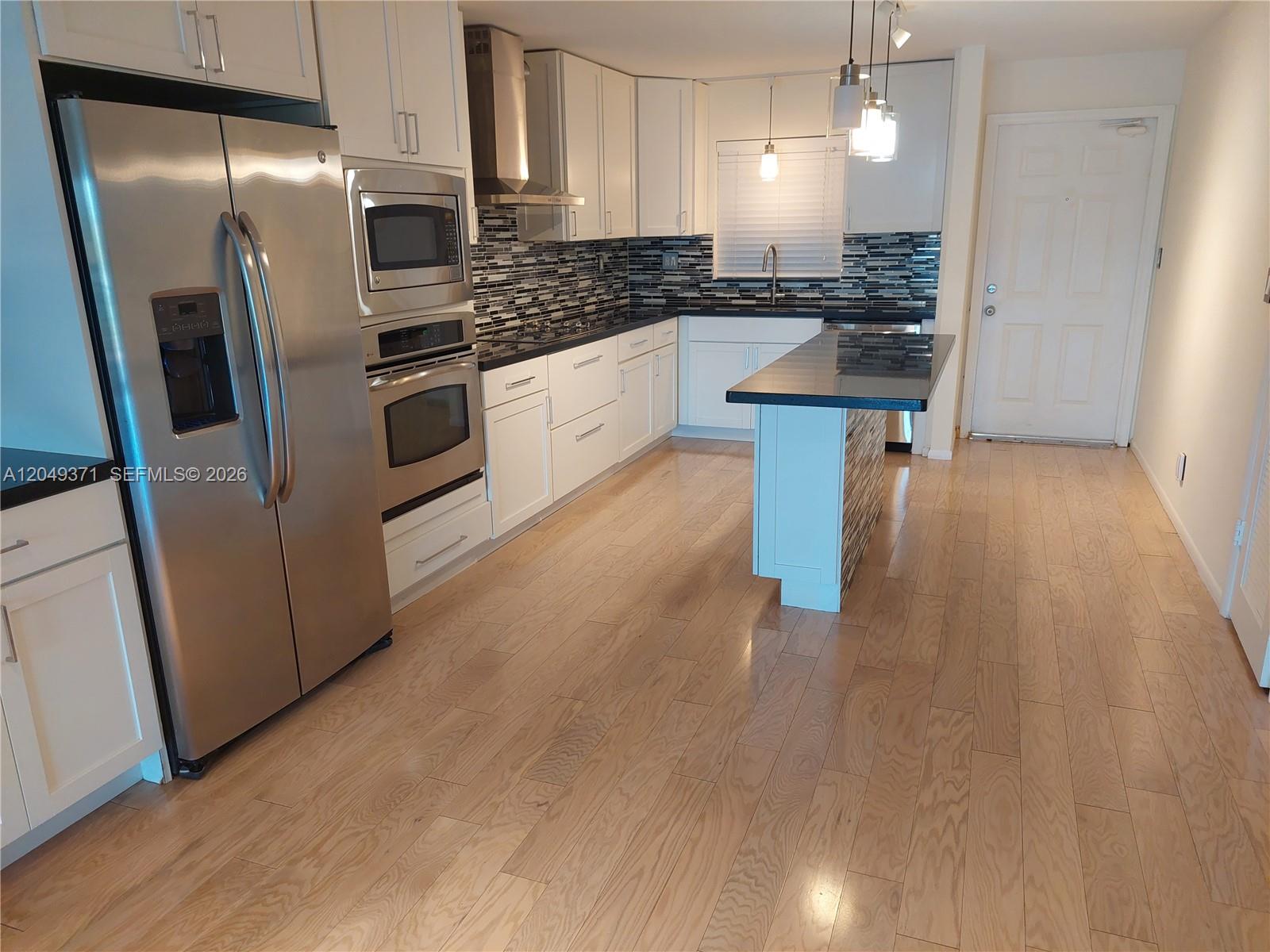 A kitchen features white cabinets, stainless steel appliances, a dark countertop, and light wood flooring — FORT LAUDERDALE, FL