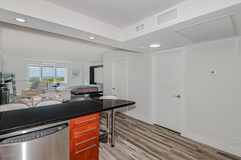 A kitchen island with a black countertop overlooks a living area and bedroom with wood-look flooring — 2301 Collins Ave # 1532, Miami Beach FL 33139, MIAMI BEACH, FL