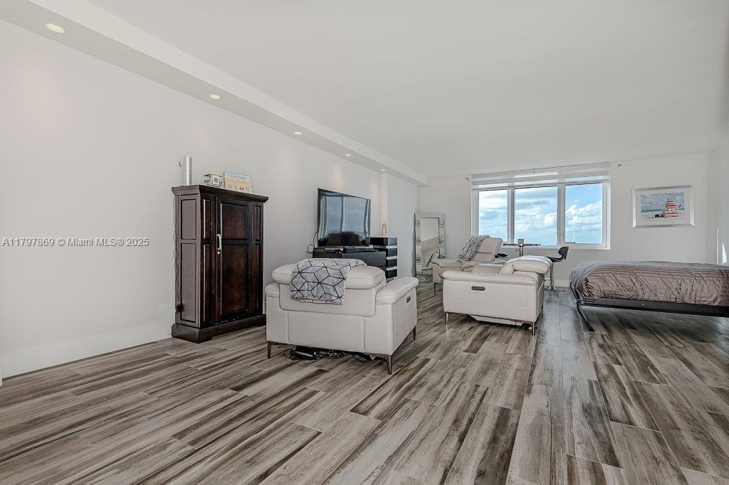 A living area features white walls, wood-look flooring, white leather furniture, and a large window — 2301 Collins Ave # 1532, Miami Beach FL 33139, MIAMI BEACH, FL