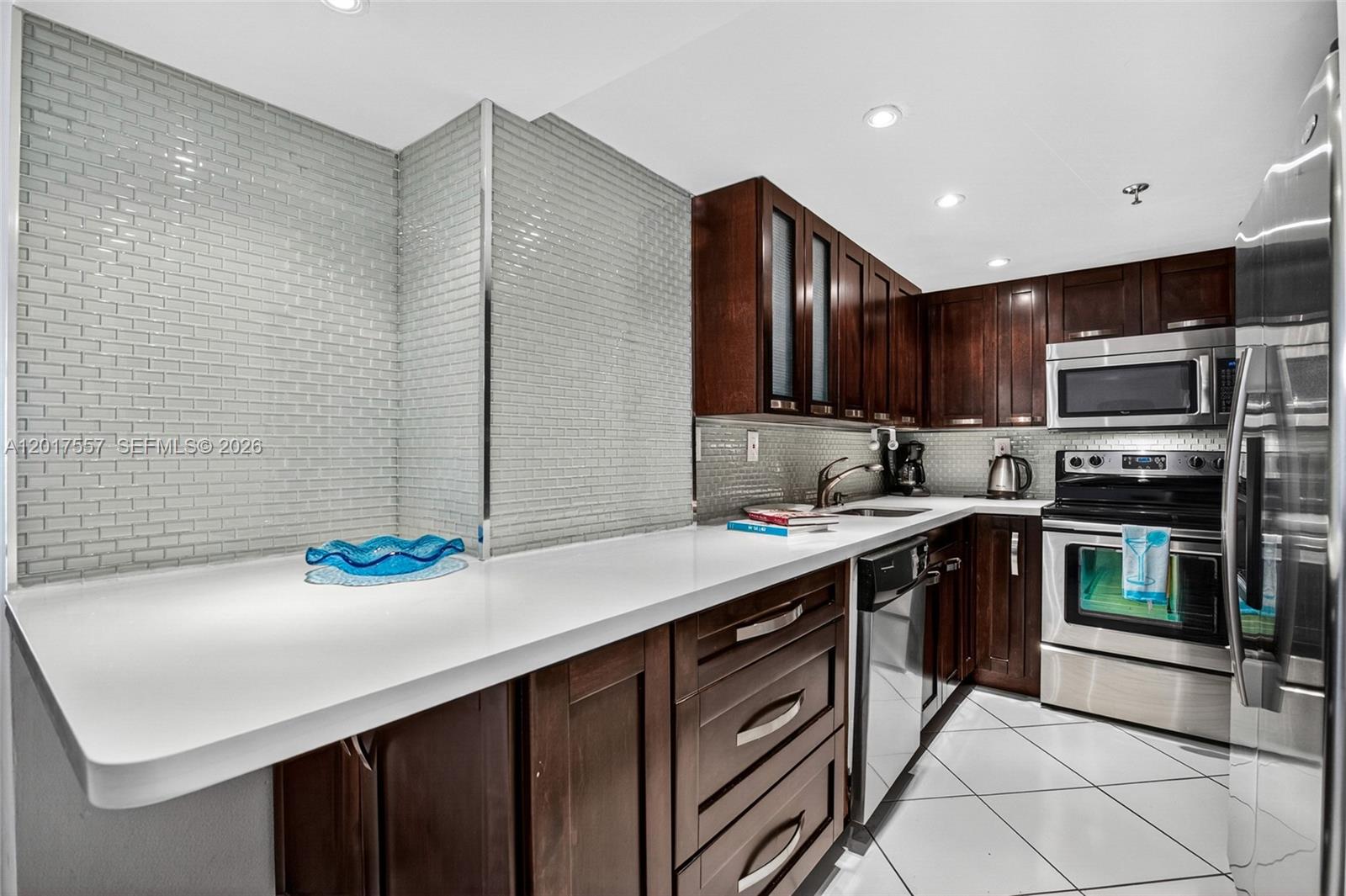 A kitchen features dark wood cabinets, white countertops, stainless steel appliances, and light gray tile — 2401 Collins Ave # 1107, Miami Beach FL 33140, MIAMI BEACH, FL