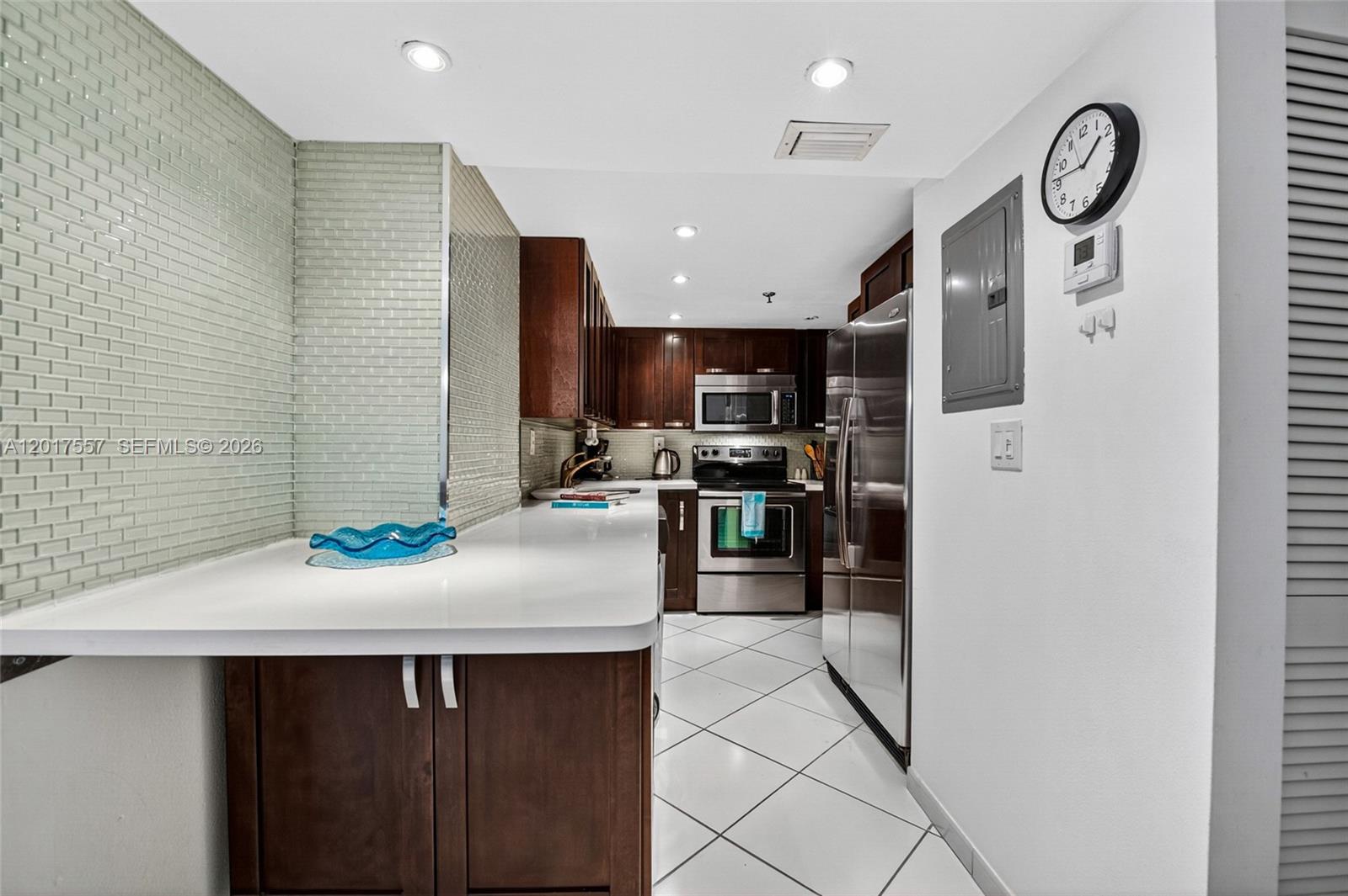 A galley kitchen features dark wood cabinets, white countertops, stainless steel appliances, and tiled flooring — 2401 Collins Ave # 1107, Miami Beach FL 33140, MIAMI BEACH, FL