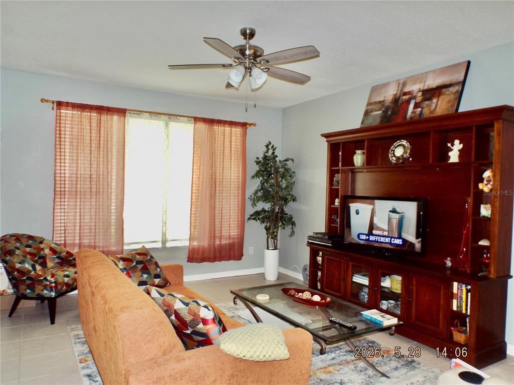 A living room features a sofa, patterned armchair, glass coffee table, and a large wooden entertainment center — 13601 FOREST LAKE DRIVE, LARGO, FL