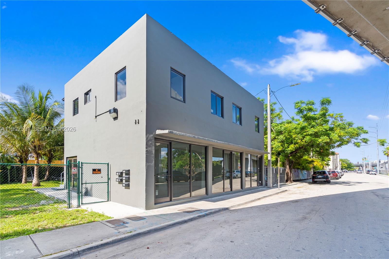 A two-story gray commercial building with large glass storefront windows sits on a paved street — 212 NW 11th St, Miami FL 33136, MIAMI, FL