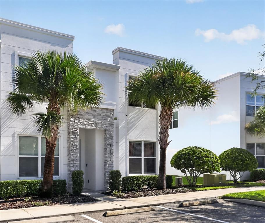 A two-story white stucco townhouse features a stone-accented entryway and two palm trees in front — 17507 HIDDEN FOREST DRIVE, CLERMONT, FL