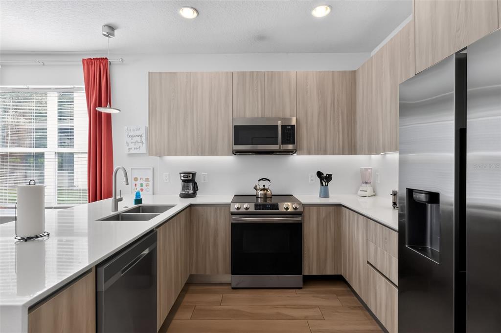 A modern kitchen features light wood cabinets, stainless steel appliances, and white quartz countertops — 17507 HIDDEN FOREST DRIVE, CLERMONT, FL