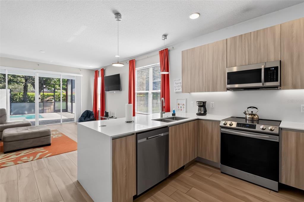 A modern kitchen with light wood cabinets, stainless steel appliances, and a white quartz island — 17507 HIDDEN FOREST DRIVE, CLERMONT, FL