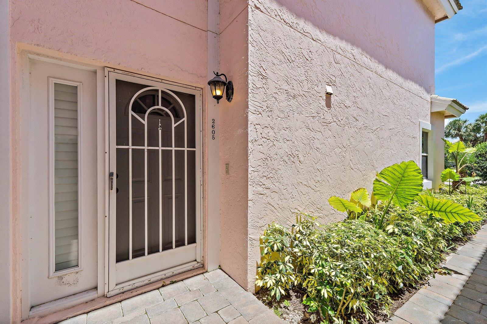 A pink stucco exterior wall features a front door with a decorative screen door — 2605 N Fairway Dr Drive N, Jupiter FL 33477, JUPITER, FL