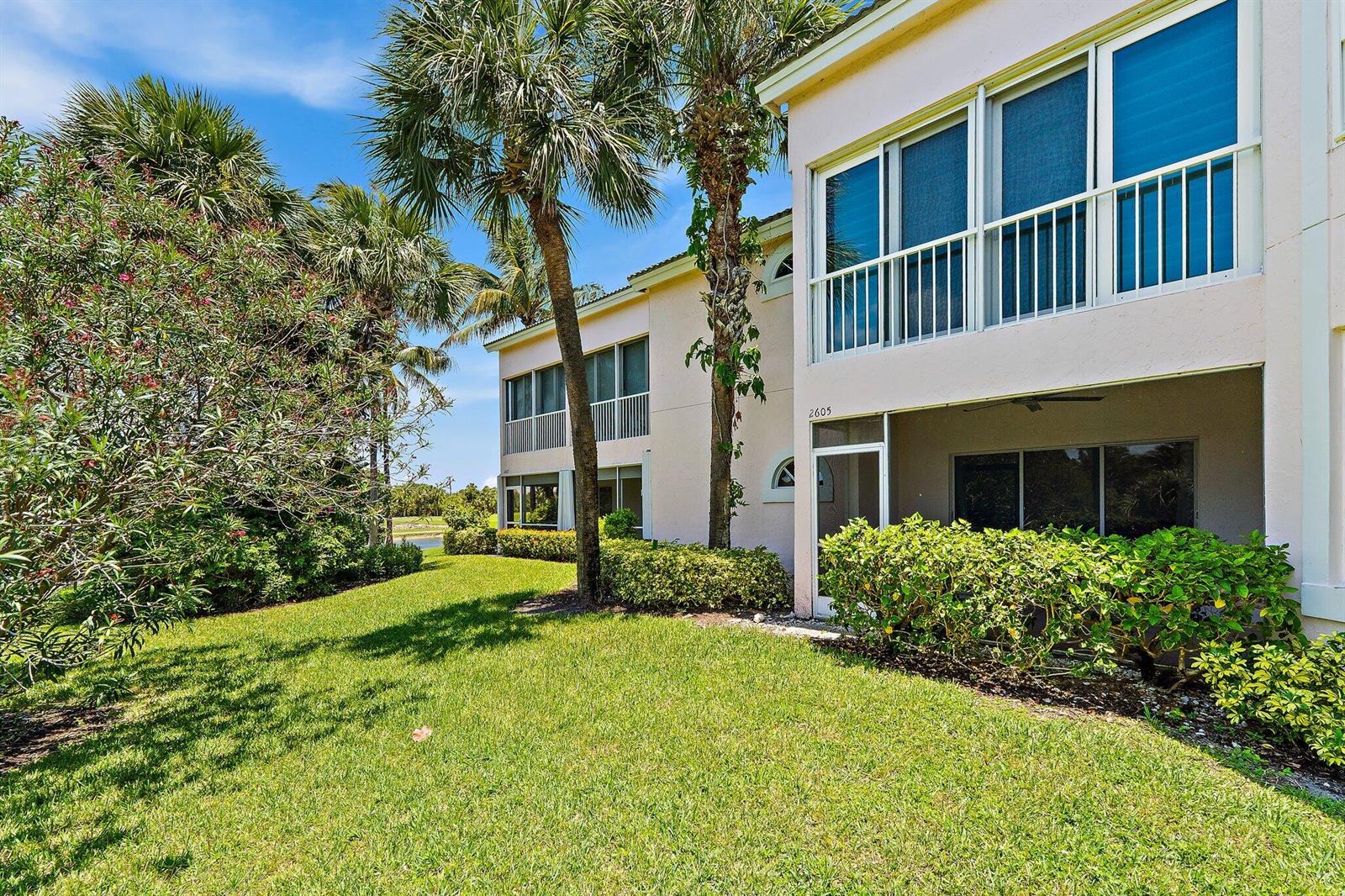 A two-story light-colored building with screened balconies and patios surrounded by grass and palm trees — 2605 N Fairway Dr Drive N, Jupiter FL 33477, JUPITER, FL