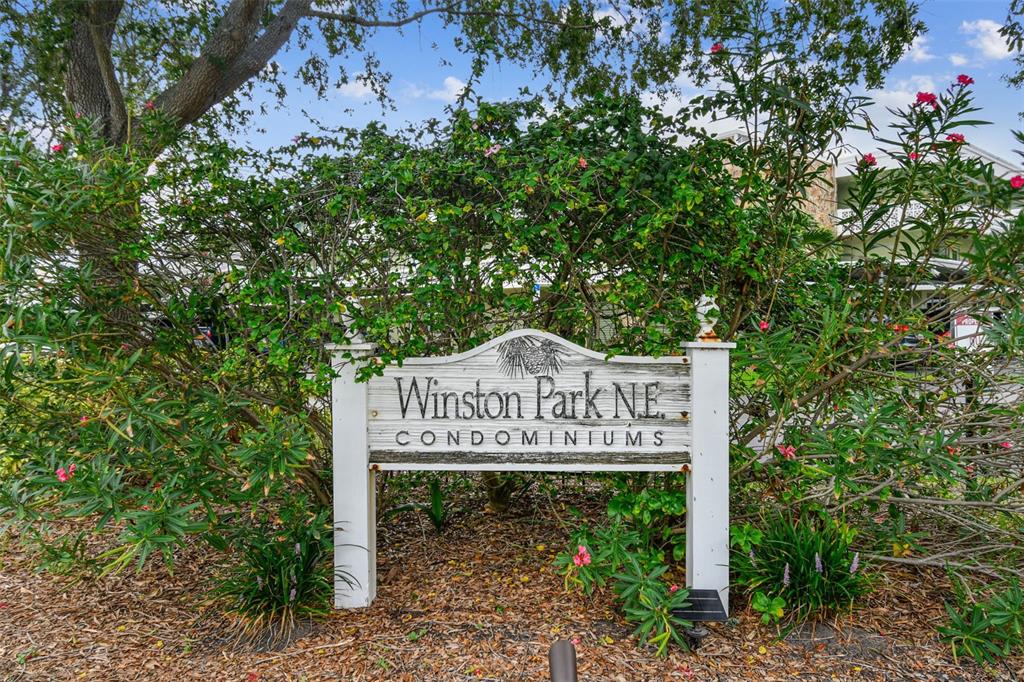 A wooden sign for Winston Park N.E. Condominiums stands in front of lush green bushes — 5095 BAY STREET NE UNIT 114, ST PETERSBURG, FL