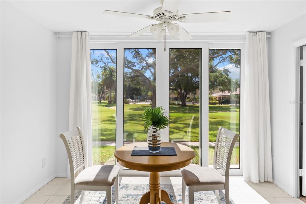 A dining area features a round wooden table, two chairs, and large windows overlooking greenery — 5095 BAY STREET NE UNIT 114, ST PETERSBURG, FL