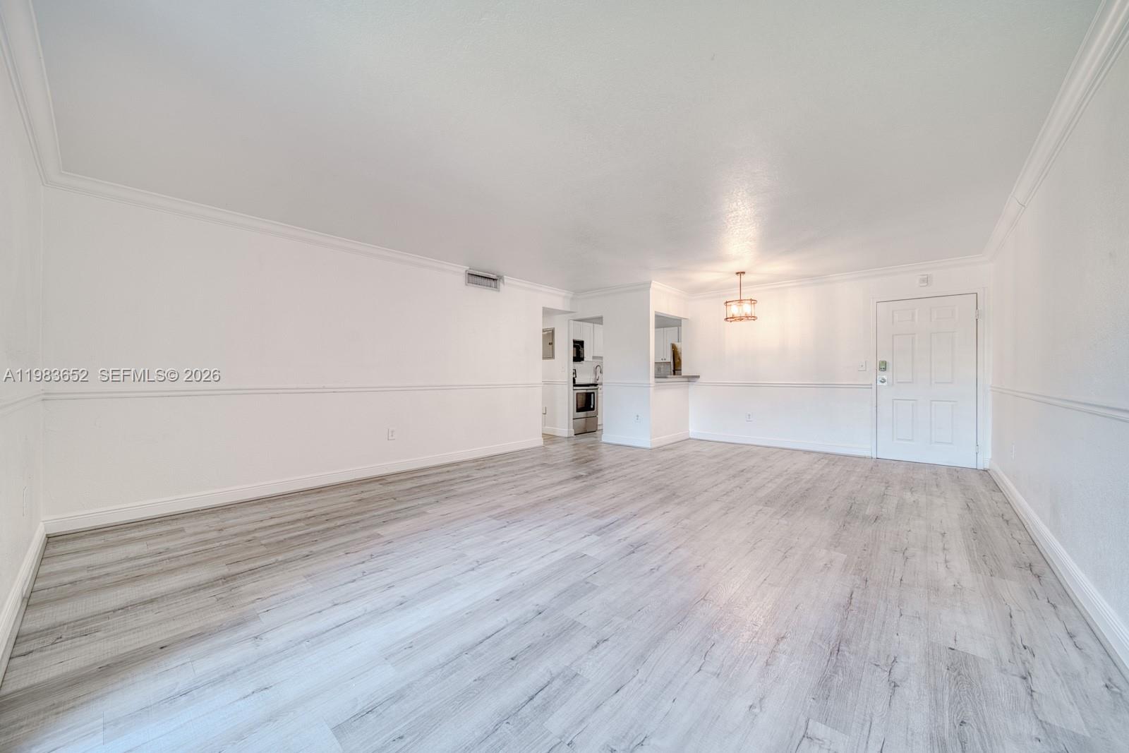 An empty living room features white walls, chair rail molding, and light gray wood-look flooring — 9459 SW 76th St # R5, Miami FL 33173, MIAMI, FL