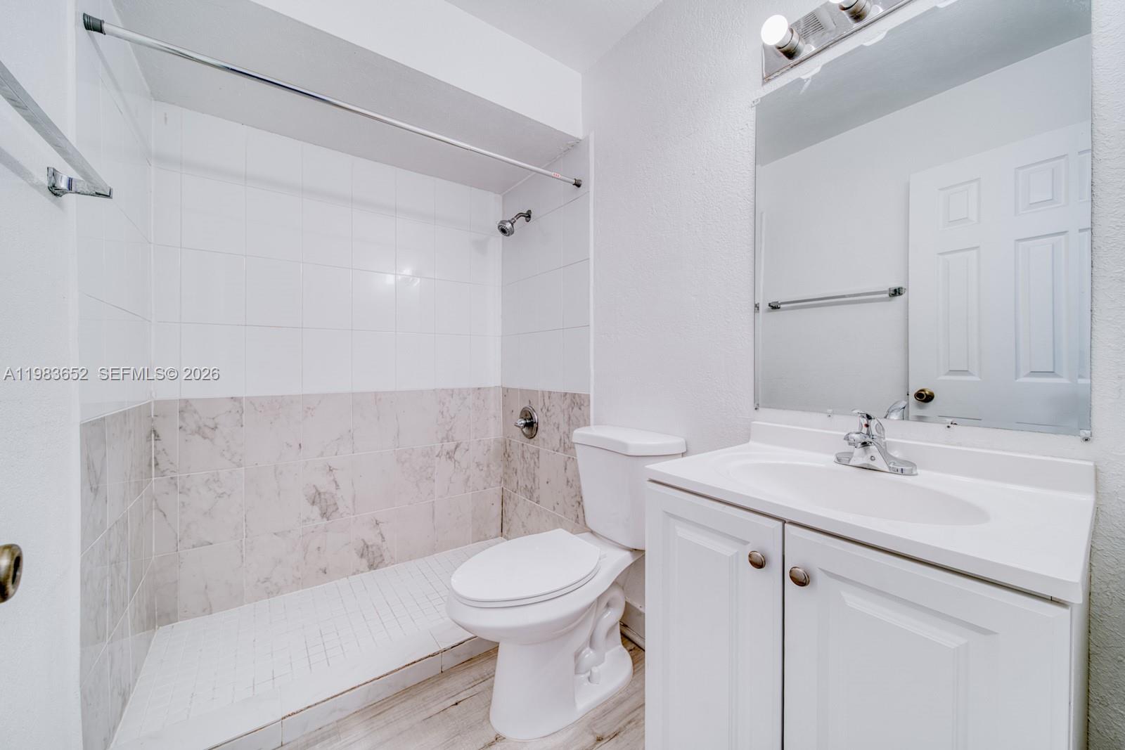 A bathroom features a white vanity, a toilet, and a shower with marble-patterned tile walls — 9459 SW 76th St # R5, Miami FL 33173, MIAMI, FL