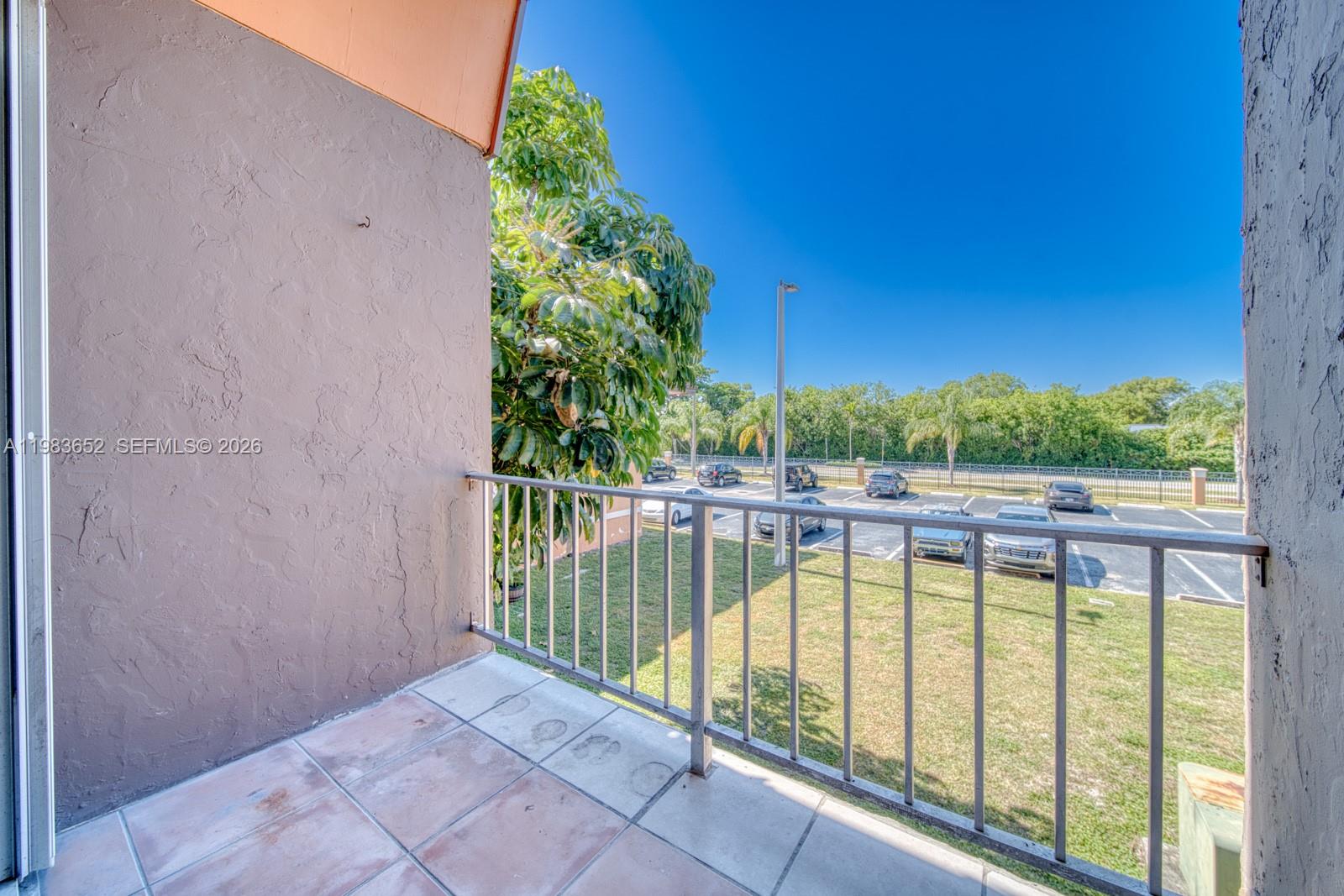 A balcony with tiled flooring and a metal railing overlooks a parking lot and trees — 9459 SW 76th St # R5, Miami FL 33173, MIAMI, FL