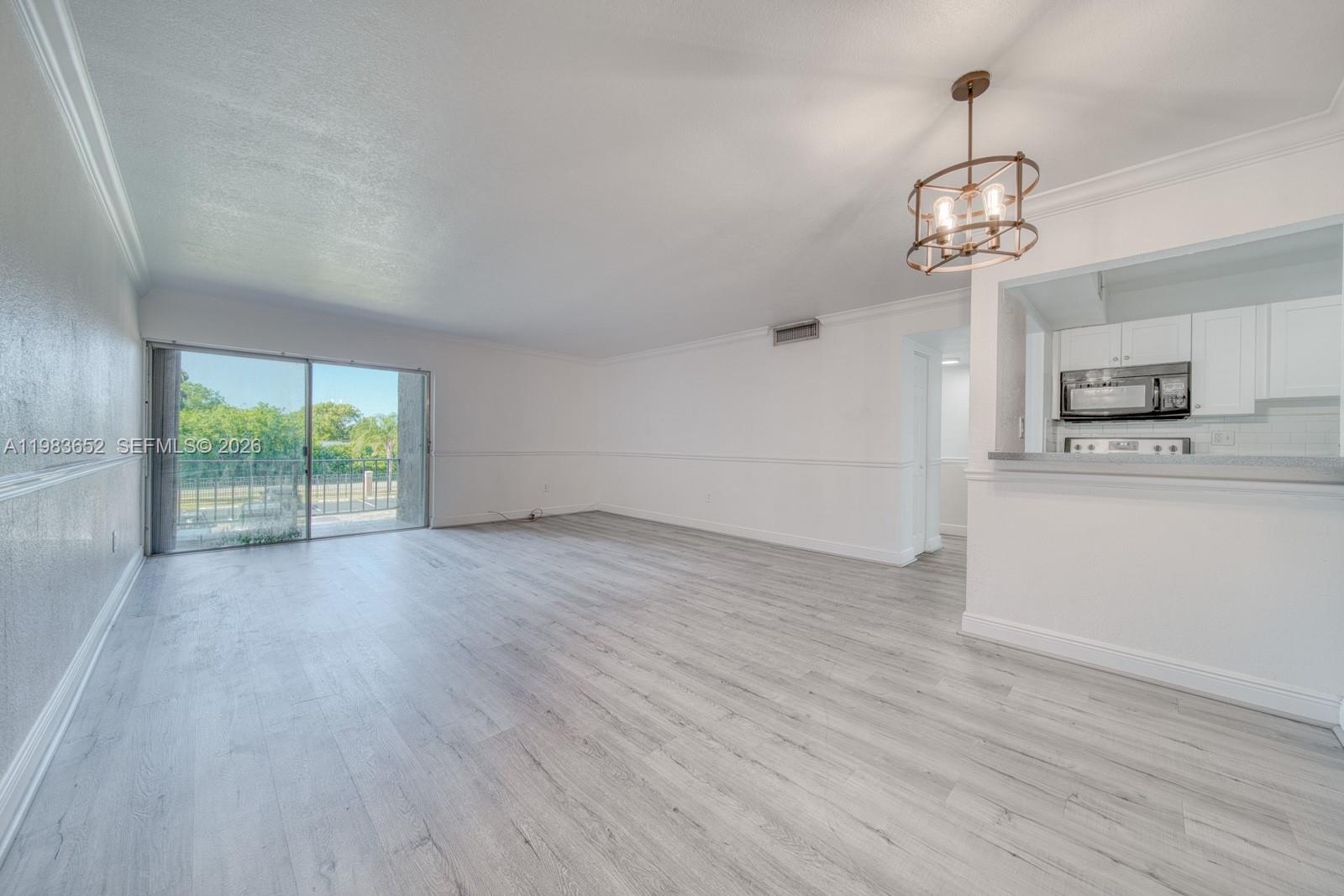 An empty living room with light wood-look flooring, white walls, and a sliding glass door — 9459 SW 76th St # R5, Miami FL 33173, MIAMI, FL