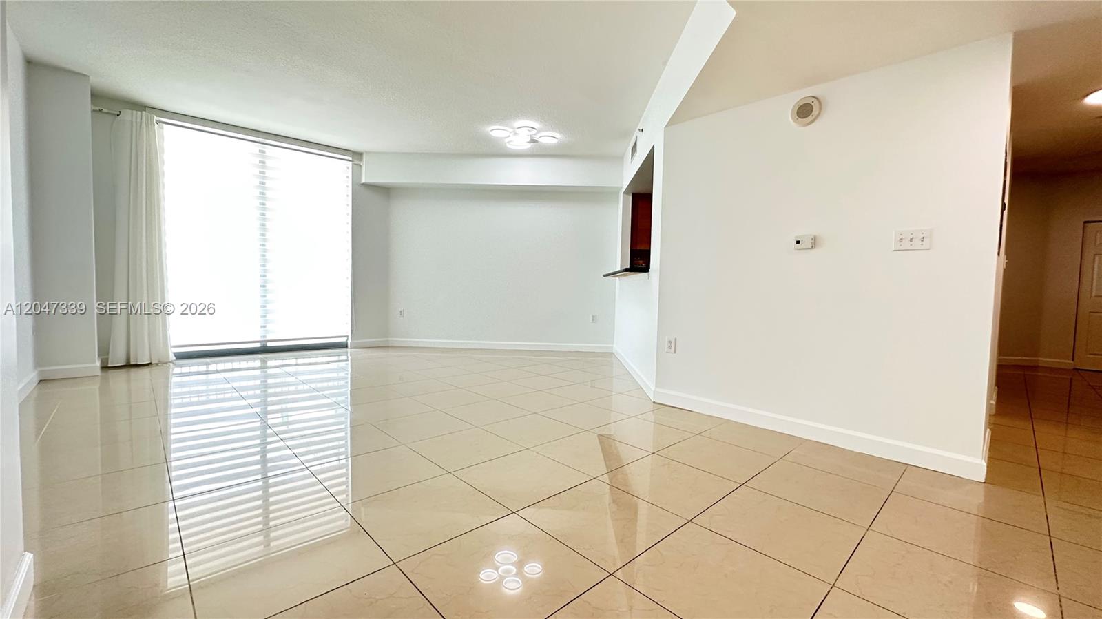 An empty living area features light-colored tile flooring, white walls, and a large window — 140 S Dixie Hwy # 808, Hollywood FL 33020, HOLLYWOOD, FL