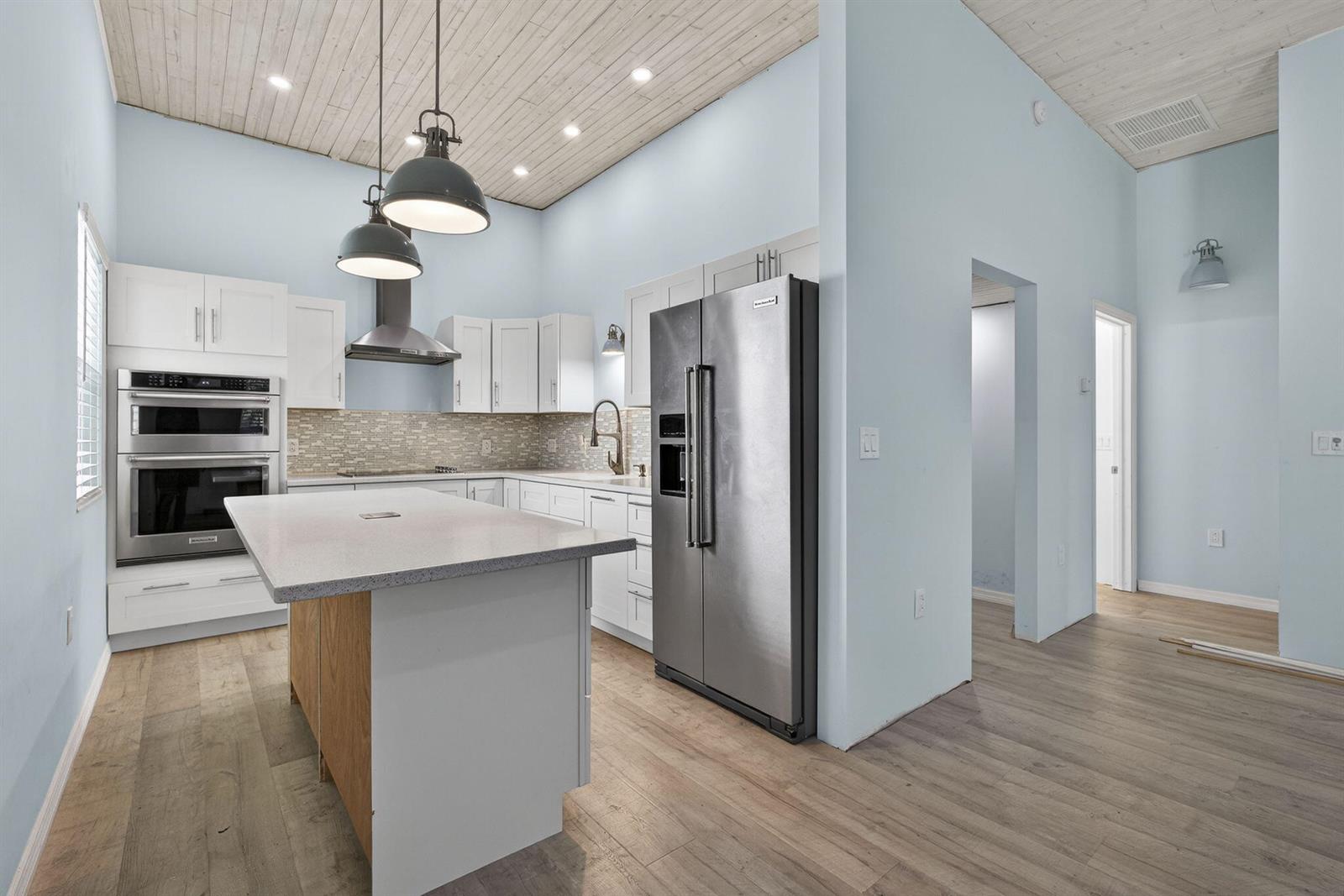 A kitchen features white cabinets, stainless steel appliances, a center island, and light wood flooring — 15399 N 61st Pl Place N, FL 33470, FL