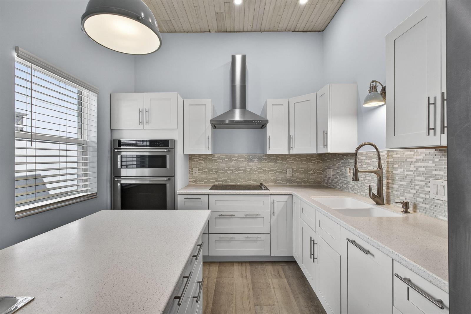 A kitchen features white cabinetry, stainless steel appliances, a quartz island, and a wood ceiling — 15399 N 61st Pl Place N, FL 33470, FL