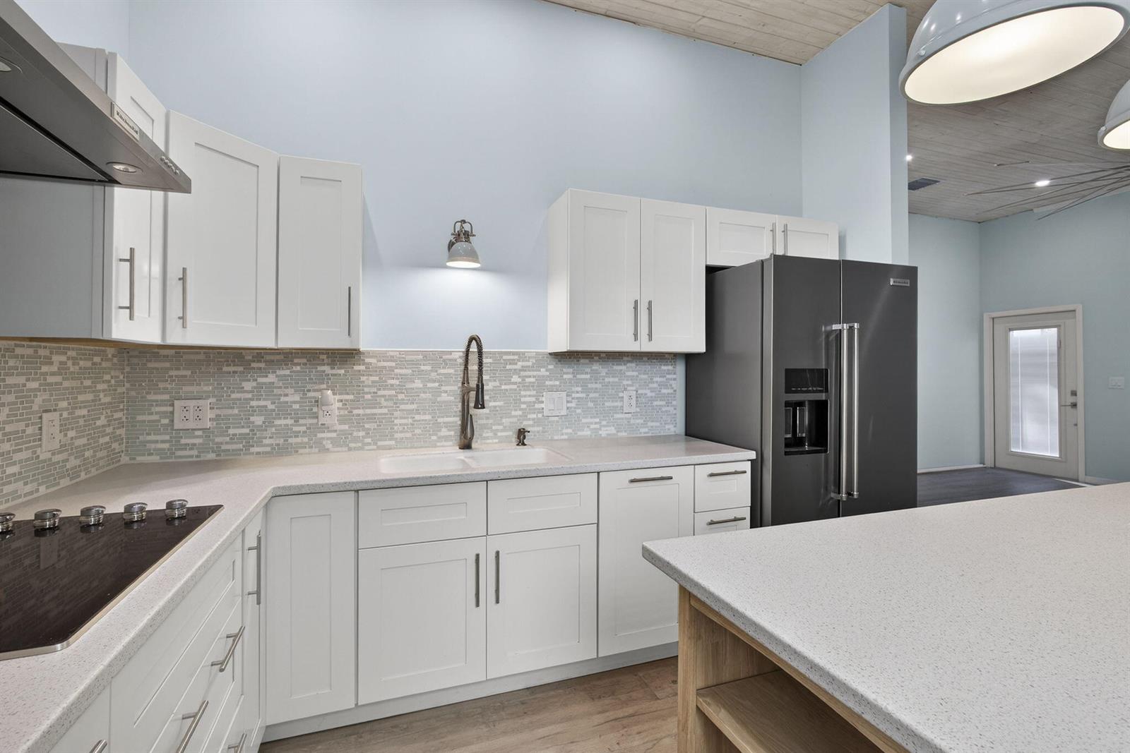 A kitchen features white cabinets, a light-colored mosaic backsplash, quartz countertops, and stainless appliances — 15399 N 61st Pl Place N, FL 33470, FL