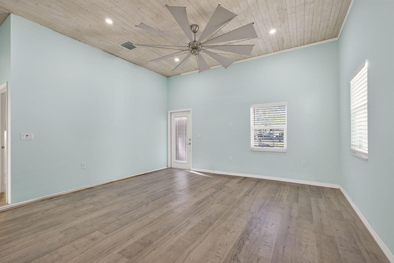 An empty room with light blue walls, wood-look flooring, and a large windmill ceiling fan — 15399 N 61st Pl Place N, FL 33470, FL