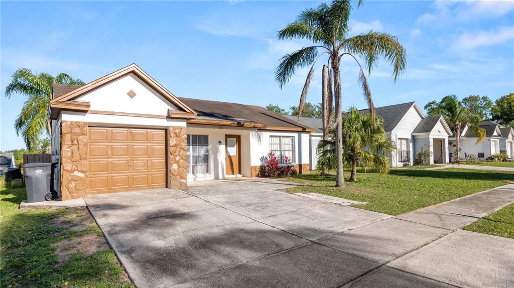 A single-story house with a brown garage door, stone accents, and a palm tree — 303 REGAL PARK DRIVE, VALRICO, FL