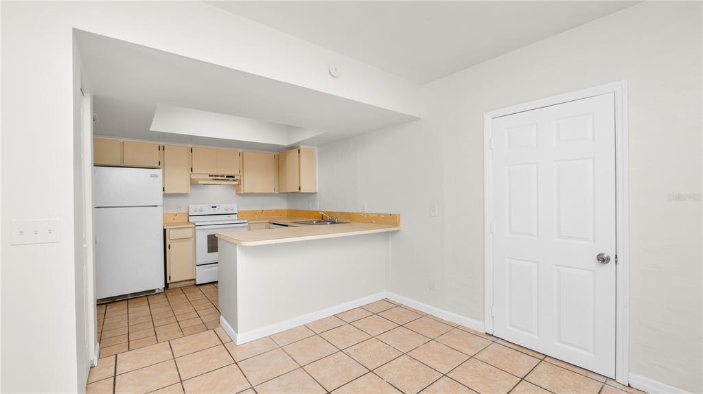 A kitchen with white appliances, light wood cabinets, and tile flooring features a breakfast bar — 303 REGAL PARK DRIVE, VALRICO, FL