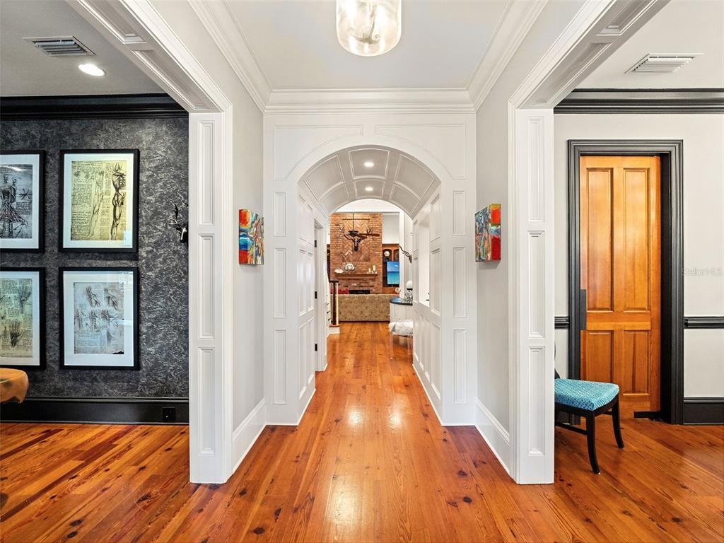 A hallway with hardwood floors leads through a white arched entryway toward a brick fireplace — 1600 LEGION DRIVE, WINTER PARK, FL